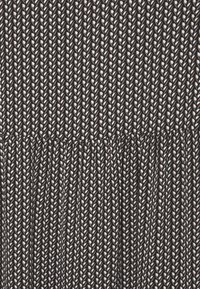 Svart tyg med ett vitt fjädermönster; plisserad design vid midjan, vilket skapar en texturerad look. Diskret lyster framhäver detaljer.