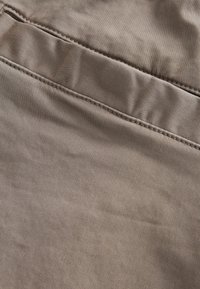 Tissu beige à texture lisse, présentant un détail de poche plate et une couture subtile le long des bords.