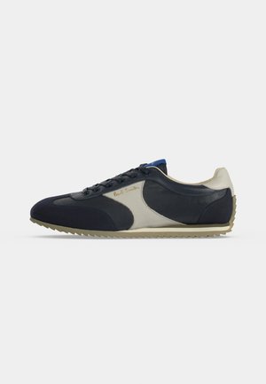 Baskets profil bas avec panneaux en cuir noir et blanc, semelle beige, lacets à l’avant et logo "Paul Smith" sur le panneau latéral.