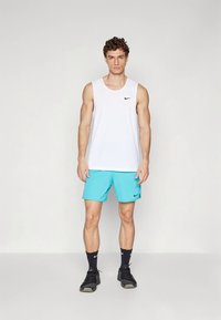 Bílý tílko bez rukávů s černým logem Nike, doplněné tyrkysovými šortkami s elastickým pasem, černými ponožkami a černými teniskami.