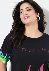 Camiseta negra con patrones de llamas coloridas en las mangas, con el texto "Estoy en llamas" en acentos similares a estrellas en el pecho.