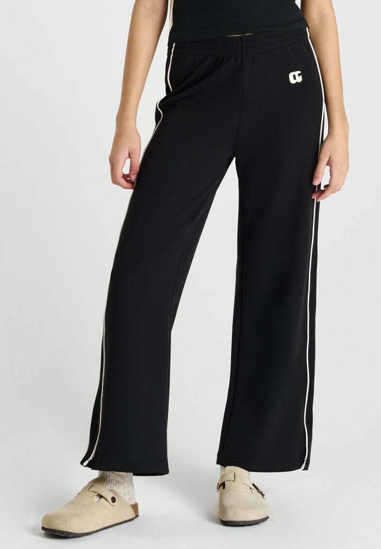 Zwarte wijdgevallen sweatpants van zachte stof, met witte zijstrepen en een geborduurd logo op de heup. Geaccentueerd met casual schoeisel.