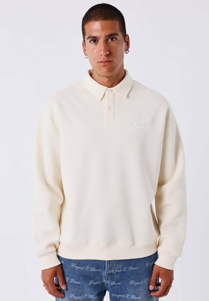 Crèmekleurige polo sweatshirt met lange mouwen, twee knopen bij de kraag en een geborduurd logo op de borst. Zachte textuur, ontspannen pasvorm.
