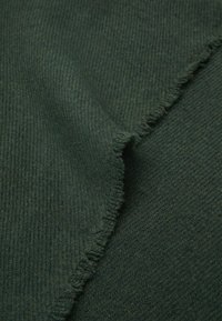 Dark green knit fabric with a ribbed texture and frayed edges, showcasing a soft, woven appearance and a rich color depth.