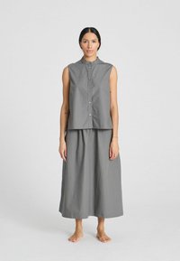 Top gris sin mangas con botones y un cuello alto, combinado con una falda larga a juego. El material parece ligero y ligeramente texturizado.