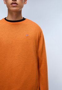 Maglione lavorato a maglia arancione con colletto nero, caratterizzato da una piccola bandiera ricamata sul petto. Tessuto morbido, vestibilità comoda.