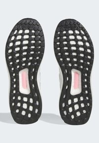 Sko sulor med en svart gummibas som har cirkulära och hexagonala mönster, samt ett centralt genomskinligt område med en rosa accent.