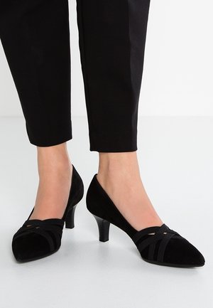 Chaussures à talons hauts en suede noir avec un bout pointu, présentant des sangles en tissu croisées sur le devant et un talon stiletto fin.