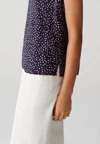 Top senza maniche blu navy con un motivo a macchie rosa e bianche, dotato di spacco laterale per maggior comodità. Abbinarlo a pantaloni bianchi a gamba dritta.