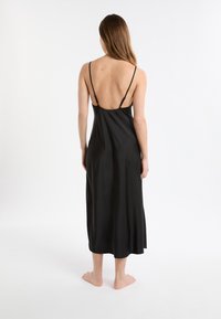 Vestido lencero de satén negro con tirantes finos ajustables, de longitud media, textura suave y diseño con escote bajo en la espalda.