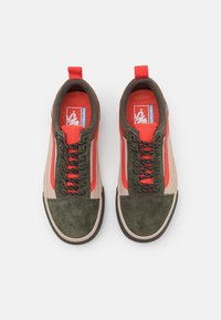 Röda och gröna mockaskor med en beige ovandel, svarta snören och en röd dragflik. Har en blå logotyp på tungan. Texturerad design.