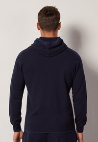 Marinblå hoodie med långa ärmar, ribbade mudd och en huva med snodd. Mjuk tyg med slät textur, inga synliga mönster eller accenter.