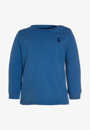 Modrá dlouhá rukávová košile vyrobená z bavlny s kulatým výstřihem. Obsahuje malé, tmavé logo na hrudi a ribbované manžety.