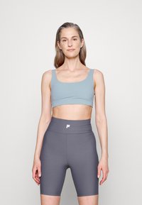 Sutiã desportivo azul claro com decote em forma de barco, combinado com calções de ciclismo cinzentos, altos e com nervuras, apresentando um logótipo branco na cintura.
