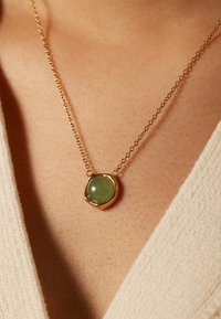 Gouden ketting met een ronde groene edelstenen hanger in een gestructureerde, onregelmatige vorm, hangend aan een delicate ketting.