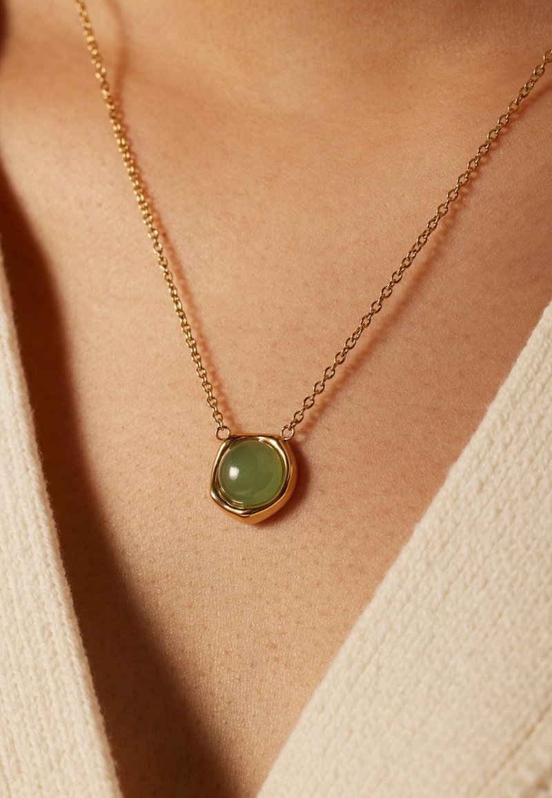 Gouden ketting met een ronde groene edelstenen hanger in een gestructureerde, onregelmatige vorm, hangend aan een delicate ketting.