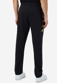 Zwarte sweatpants met een elastische tailleband en boorden, voorzien van een gouden logo-detail langs de zijkant, gemaakt van zachte stof.