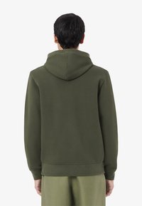 Felpa verde oliva con cappuccio regolabile, polsini e orlo a coste. Tessuto liscio, presenta cuciture minime sul retro.