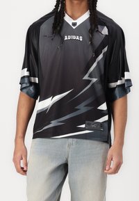 Mustavalkoinen lyhythihainen pelipaita, jossa on voimakkaat salaman kuvastot, verkkokangas, ja Adidaksen logo rinnassa, viimeistelty tarralla helmassa.