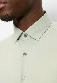 Hellgrünes Kurzarmhemd mit klassischem Kragen, ausgestattet mit zwei runden Knöpfen und einem glatten, strukturierten Stoff.