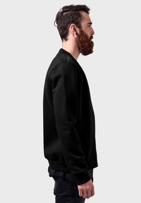 Svart hettegenser med et enkelt design, rund hals og lange ermer. Stoffet ser mykt ut med ribbestrikkede mansjetter og nederkant.