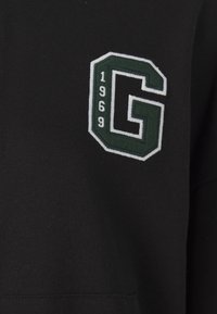 Zwarte hoodie met een geborduurde groene en witte "G" patch met daaronder "1969", met een gestructureerde stof en een sportief ontwerp.