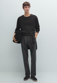 Dark, textured long-sleeve sweater paired with dark, tailored trousers. Presented with a folded garment and casual shoes. Neutral background.