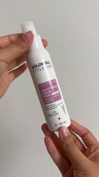 Hände halten eine weiße Flasche Goldwell StyleSign Heat Styling Smoothing Serum Spray, 100 ml, für alle Haartypen.
