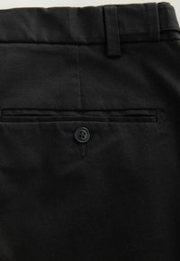 Czarne spodnie o gładkiej fakturze, z tylną kieszenią zabezpieczoną czarnym guzikem z czterema dziurkami. Klasyczny, dopasowany krój.