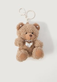 Porte-clés en peluche marron en forme d'ours en peluche avec un pendentif en forme de cœur argenté autour de son cou et des embellissements en forme d'étoile sur ses oreilles.