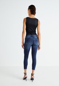 Top negro sin mangas combinado con jeans ajustados de color azul oscuro, con bolsillos traseros y detalles de cremallera, llevado con tacones de tiras.