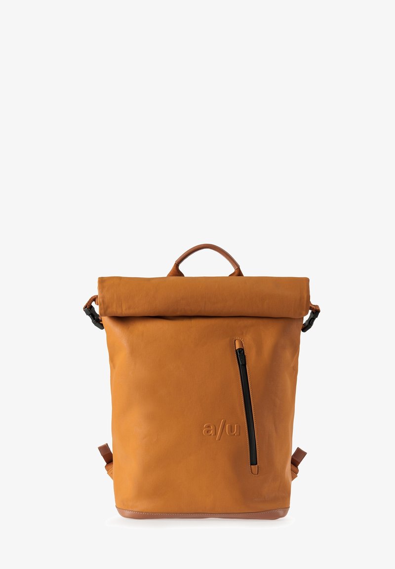 Sac à dos beige à fermeture roulante avec une poche zippée verticale et un logo "a/u" embossé sur le devant, doté d'une poignée supérieure et de bretelles ajustables.