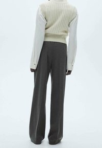 Gilet en tricot crème sur une chemise blanche à boutons, associé à un pantalon gris à jambe large. Présente une texture côtelée et une coupe décontractée.