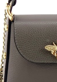 Kleine grijze leren handtas met een gestructureerde afwerking, gouden hardware accenten en een decoratief gouden bijembleem op de voorklep.