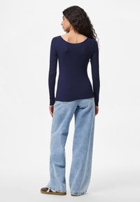 Tumedast sinise long-sleeve ribaga topp, millel on avatud seljaosa, ning kerged helesinised laiad püksid, mis on veidi kulunud ning pruunid jalatsid.