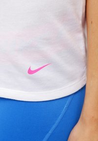 Camiseta de algodón blanca con el logo de Nike en rosa en el lado izquierdo, combinada con leggins deportivos azules que presentan un diseño elegante y detalles en costura.