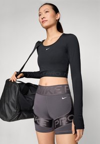 Top scurt negru cu mânecă lungă și decolteu rotund; pantaloni scurți gri cu talie înaltă și bandă contrastantă neagră; model purtând o geantă neagră.