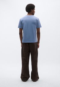 Γαλάζιο κοντομάνικο μπλουζάκι με κανονική εφαρμογή, συνδυασμένο με φαρδιά, σκούρα καφέ παντελόνια από κορδόνι με πίσω τσέπες.