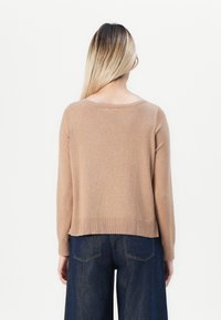 Tan, lichtgewicht trui met lange mouwen en een ronde halslijn. Kenmerkt gebreide zoom en manchetten. Draagt boven donkere denim wijduitlopende broeken.
