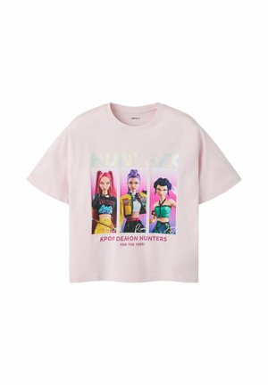 T-shirt rose clair avec trois personnages féminins animés colorés et le texte « KPOP DEMON HUNTERS FOR THE FANS ! » sur le devant.