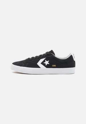 Baskets en daim noir avec des accents blancs, arborant un logo d'étoile, une semelle texturée et des lacets noirs. Design simple, style décontracté.
