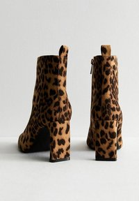 Bottines imprimé léopard avec une finition en daim texturé, talons carrés, fermetures éclairs latérales et languettes à l'arrière. Palette de couleurs marron et noir.