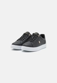 Sneakers neri in sintetico con suole in gomma bianca, dotati di chiusura con lacci, dettagli dorati e una finitura texture liscia.