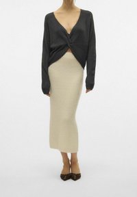 Ciemnoszary dziergany sweter z supłem z przodu, zestawiony z długą kremową teksturowaną spódnicą. Brązowe buty na obcasie dopełniają strój.