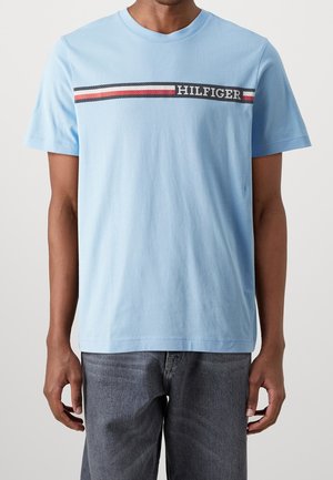 Jasnoniebieski bawełniany t-shirt z okrągłym dekoltem i krótkimi rękawami. Poziomy pasek z napisem "HILFIGER" w ciemnoniebieskim kolorze oraz akcentami czerwonymi i białymi.