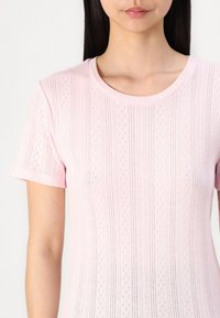 Růžový pletený top s krátkým rukávem, který se vyznačuje texturovaným vzorem s vertikálními pruhy a malými diamantovými výřezy. Klasický kulatý výstřih.