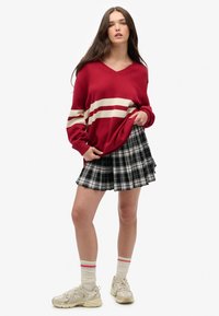 Rød striktrøje med hvide striber, parret med en sort ternet plisseret miniskørt. Stylet med beige sneakers og stribede sokker.