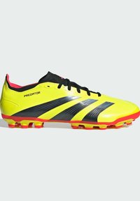 Botín de fútbol amarillo con acentos en negro y rojo, que presenta un diseño elegante, parte superior texturizada y clavos redondos en la suela para tracción.