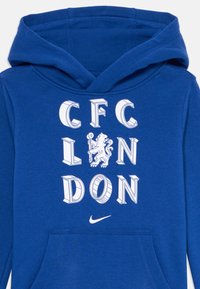 Modrá mikina s kapucí a bílými 3D blokovými písmeny, na kterých je napsáno "CFLONDON", a emblémem lva uprostřed, pod kterým se nachází malé bílé logo Nike.