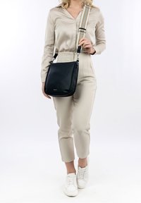 Borsa a tracolla nera in pelle con finitura testurizzata, dotata di una tracolla decorata con dettagli in argento e chiusura con zip.